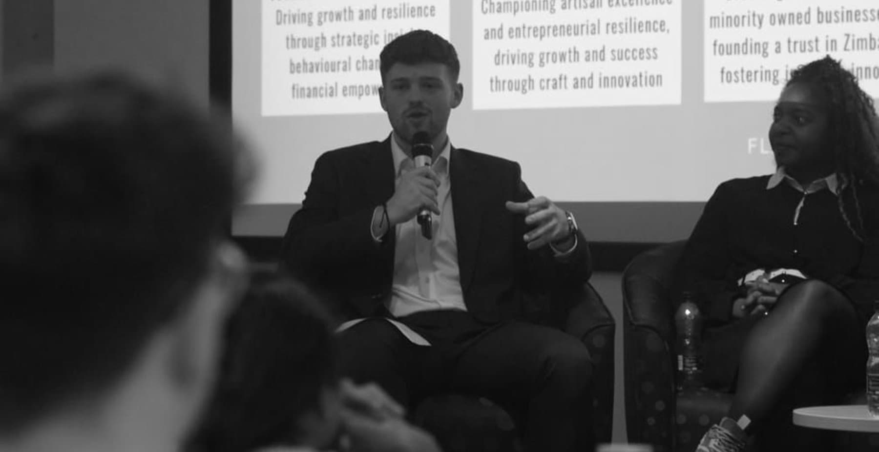 Will May speaking on a panel with a microphone, alongside another panellist